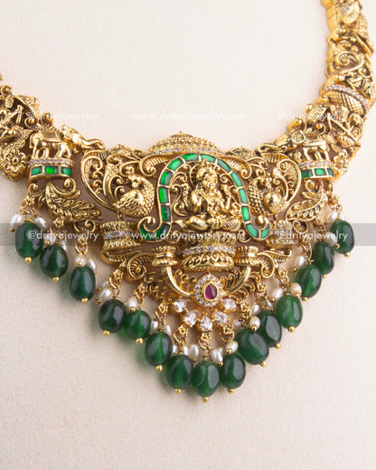 Detailed view of gold Lakshmi Devi pendant with green Jadau stones and pearl bead hangings.