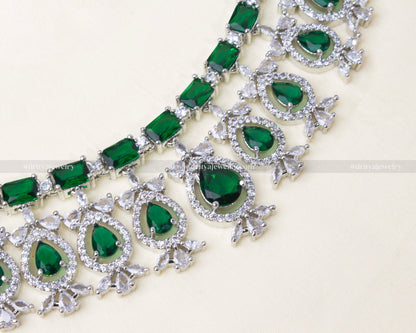 Elegant American diamond necklace set featuring green stones, matching earrings, and a maang tikka with a silver-toned finish.