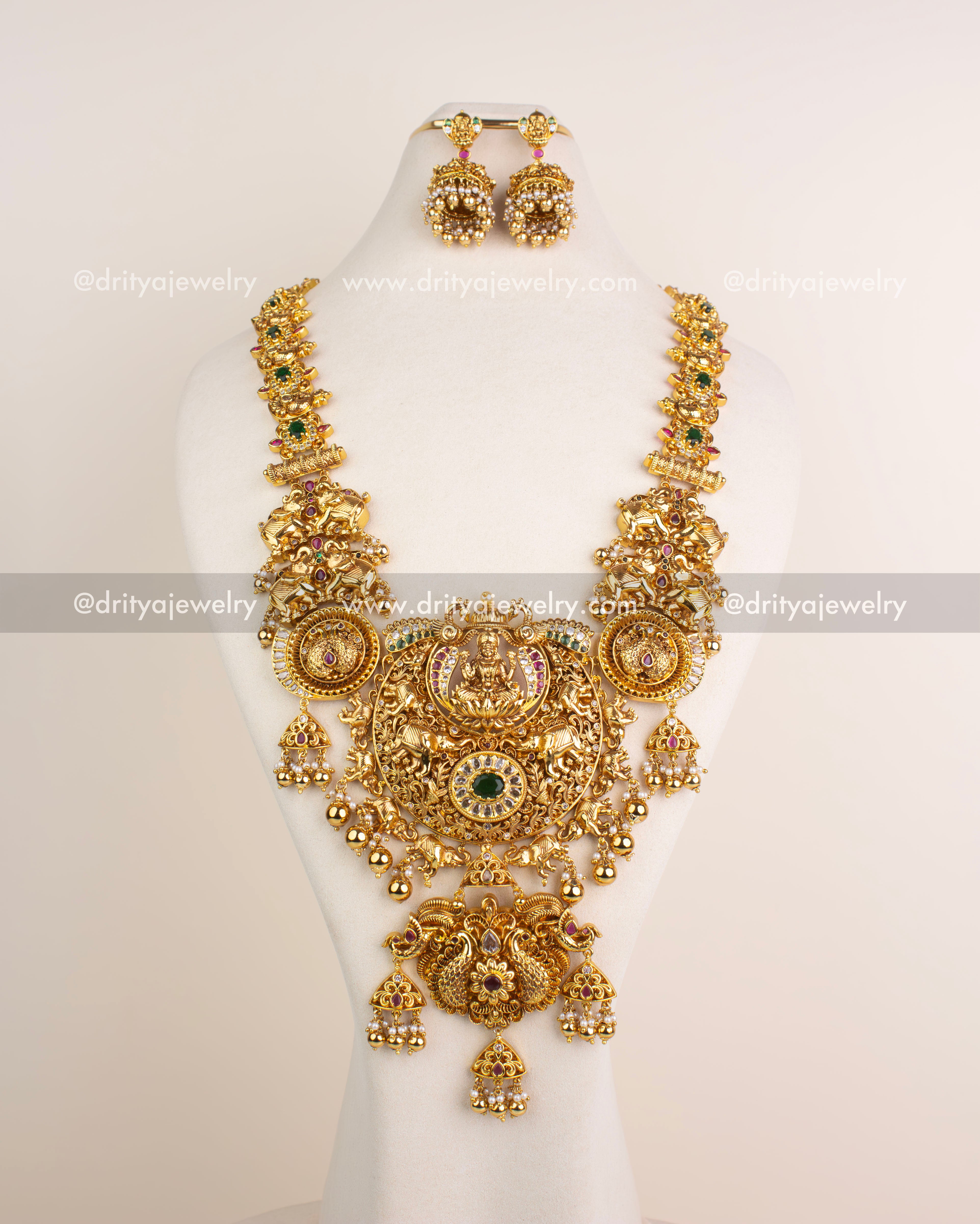 Grand bridal long necklace set with Lakshmi motif, antique polish, ruby and green stones, and matching earrings.
