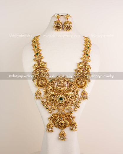 Grand bridal long necklace set with Lakshmi motif, antique polish, ruby and green stones, and matching earrings.