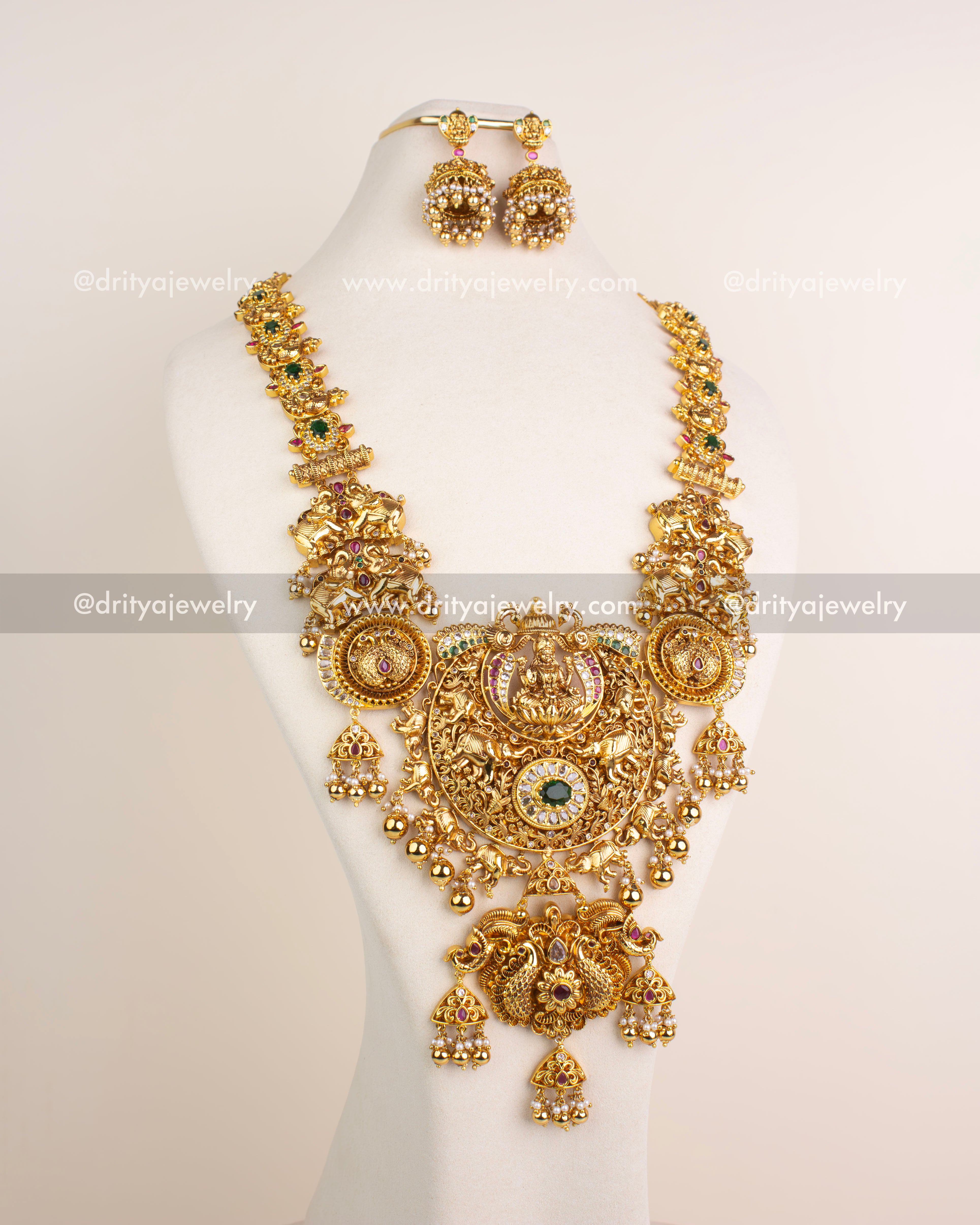 Grand bridal long necklace set with Lakshmi motif, antique polish, ruby and green stones, and matching earrings.