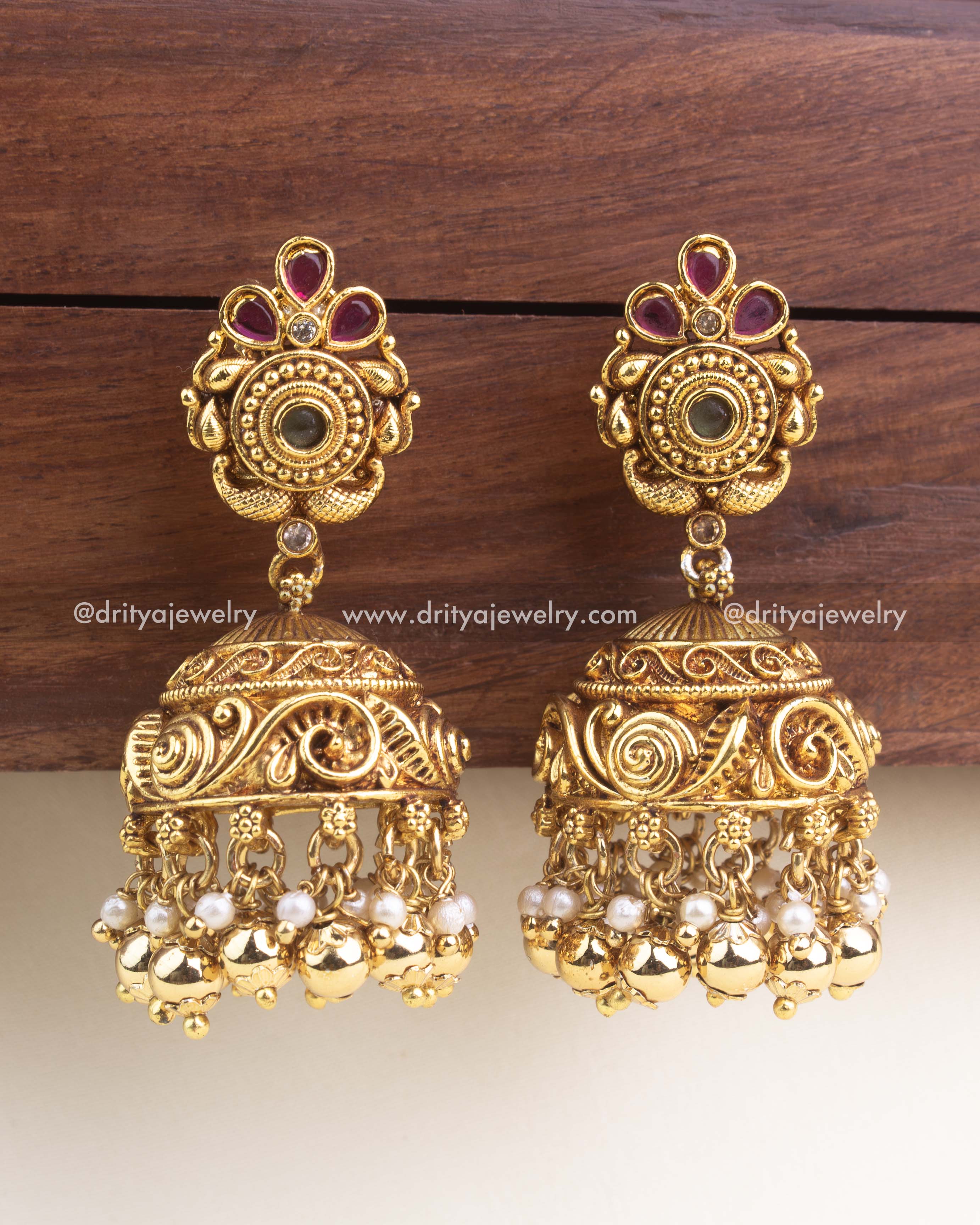 Antique gold jhumka earrings with carved stud design, ruby stones, swirl-engraved dome, and pearl-gold bead cluster drops