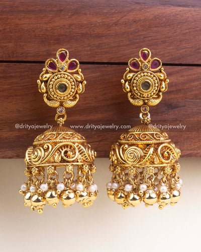 Antique gold jhumka earrings with carved stud design, ruby stones, swirl-engraved dome, and pearl-gold bead cluster drops