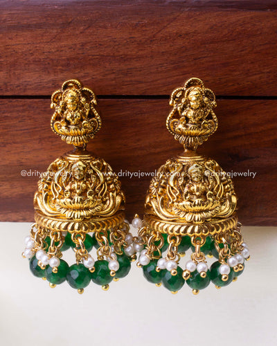 Temple-style antique Jhumkas with Goddess Lakshmi motif, emerald-green bead drops, and pearl accents.