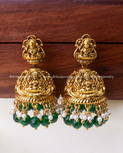 Temple-style antique Jhumkas with Goddess Lakshmi motif, emerald-green bead drops, and pearl accents.