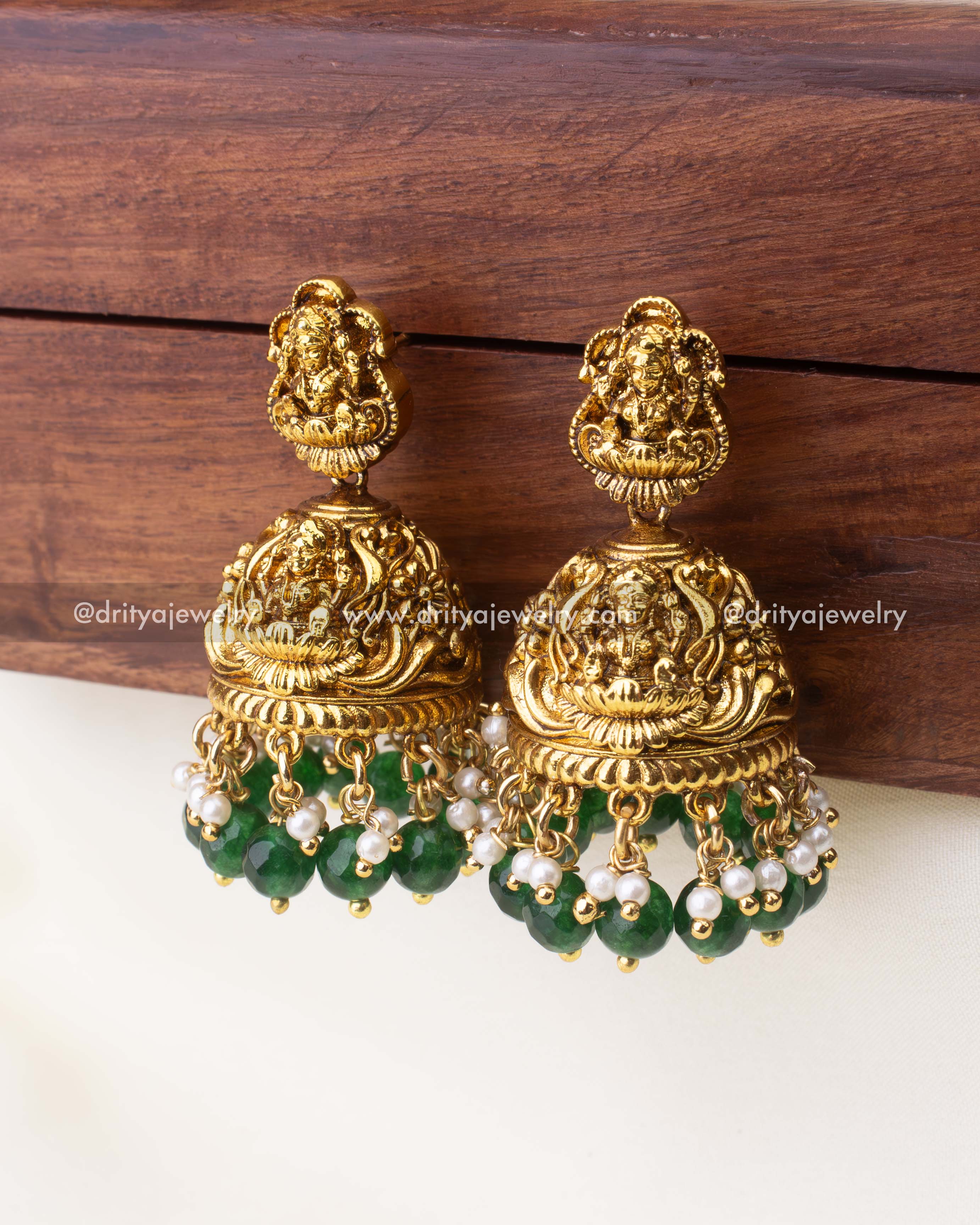 Temple-style antique Jhumkas with Goddess Lakshmi motif, emerald-green bead drops, and pearl accents.