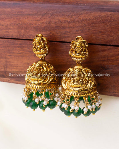 Temple-style antique Jhumkas with Goddess Lakshmi motif, emerald-green bead drops, and pearl accents.