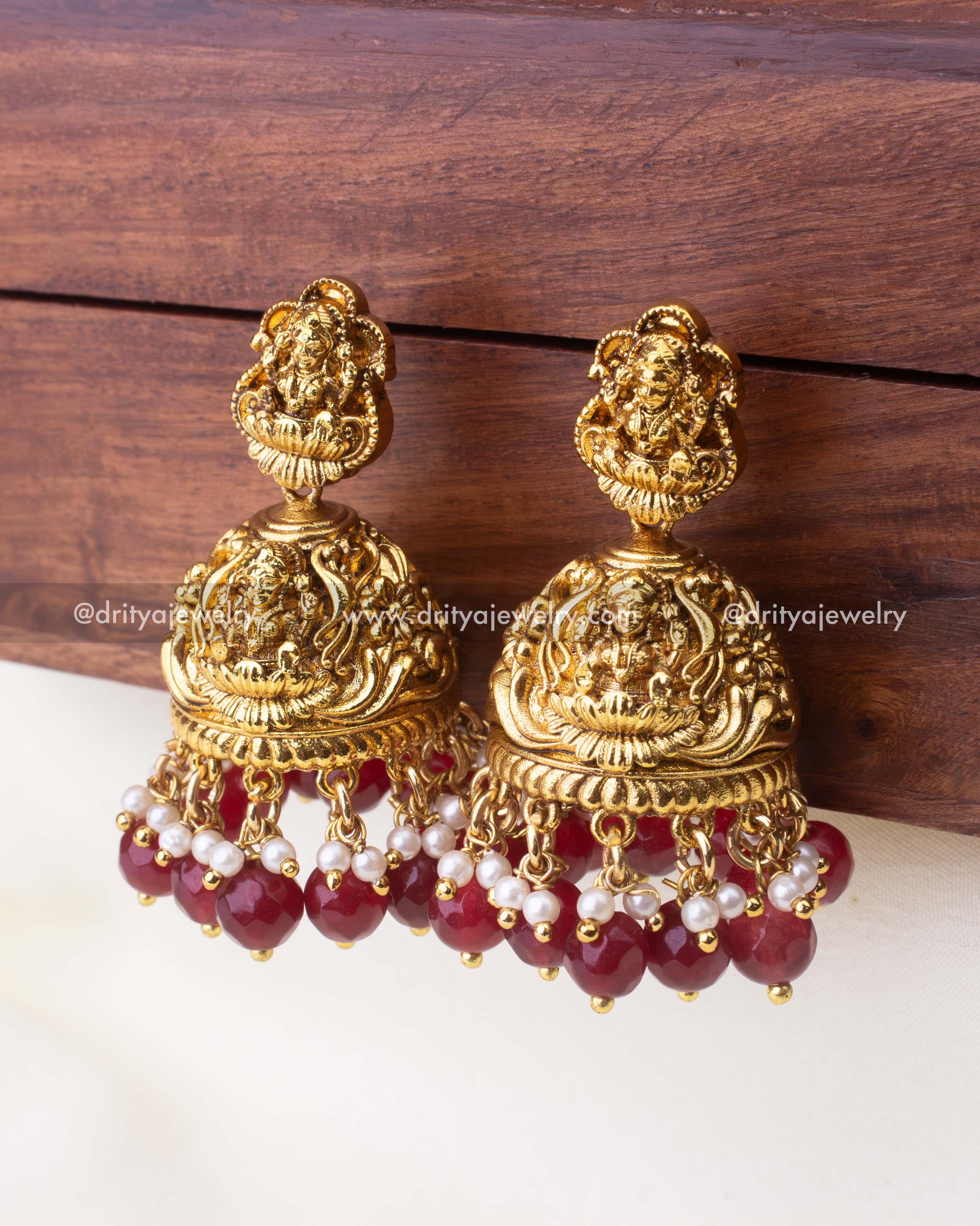 Detailed close-up of Goddess Lakshmi Jhumka earrings with ruby-red beads and pearl clusters.