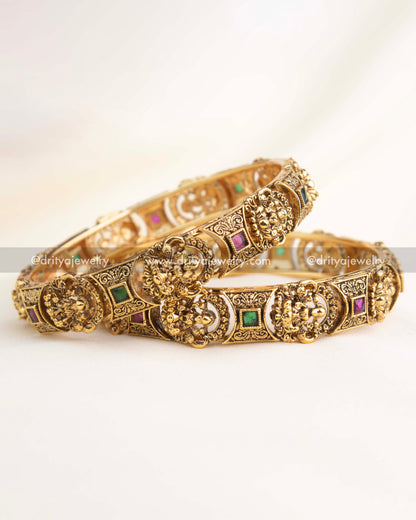 Antique gold temple bangles with intricate goddess engravings and ruby–emerald accents by Dritya Jewelry.