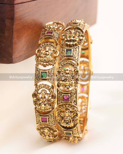 Antique gold temple bangles with intricate goddess engravings and ruby–emerald accents by Dritya Jewelry.