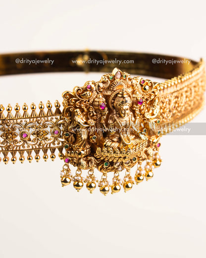 Intricate Nakshi carvings with ruby and emerald accents on antique gold waist belt.