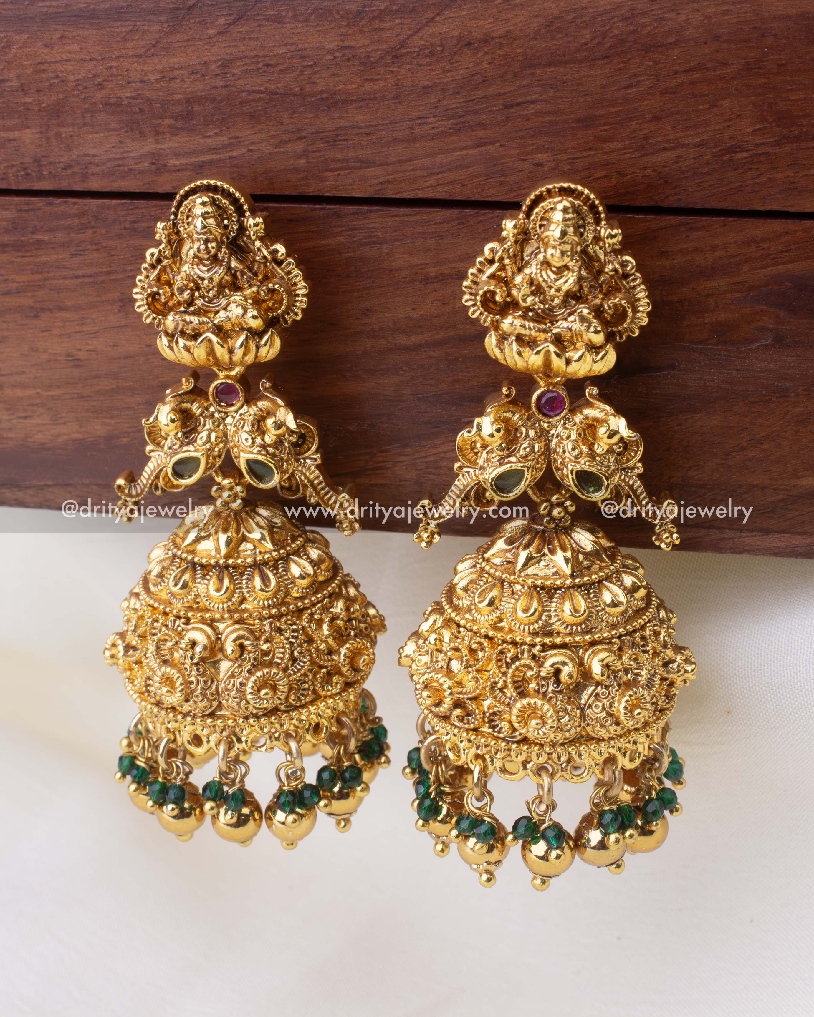 Large antique gold temple Jhumkas with Goddess Lakshmi motif and emerald bead accents.