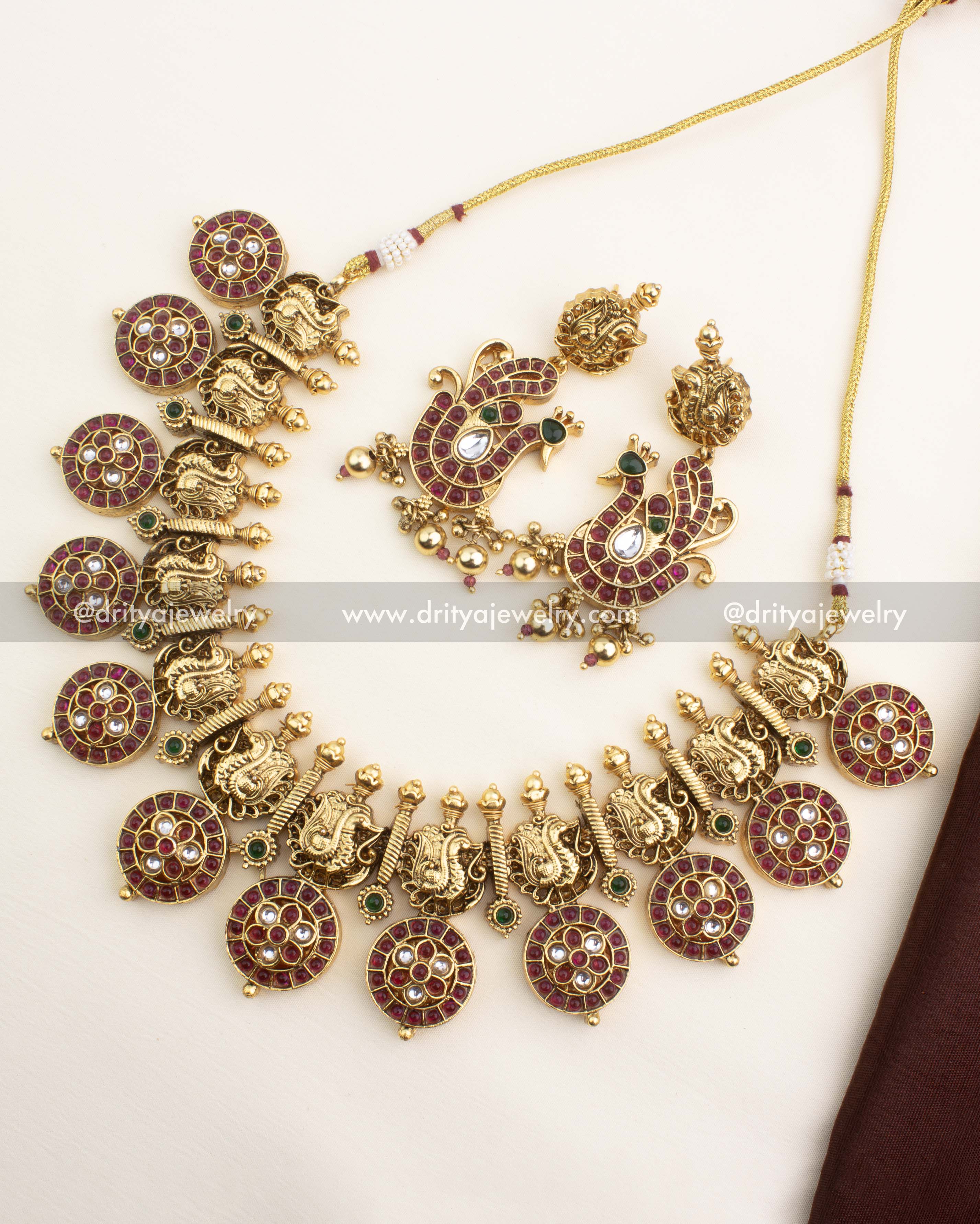 Short necklace with ruby-coloured bottu discs, gold carved motifs, and matching peacock earrings from Dritya Jewelry.