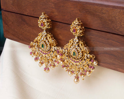 Elegant premium dangler earrings featuring green and ruby accents, cubic zirconia detailing, and hanging pearl embellishments.