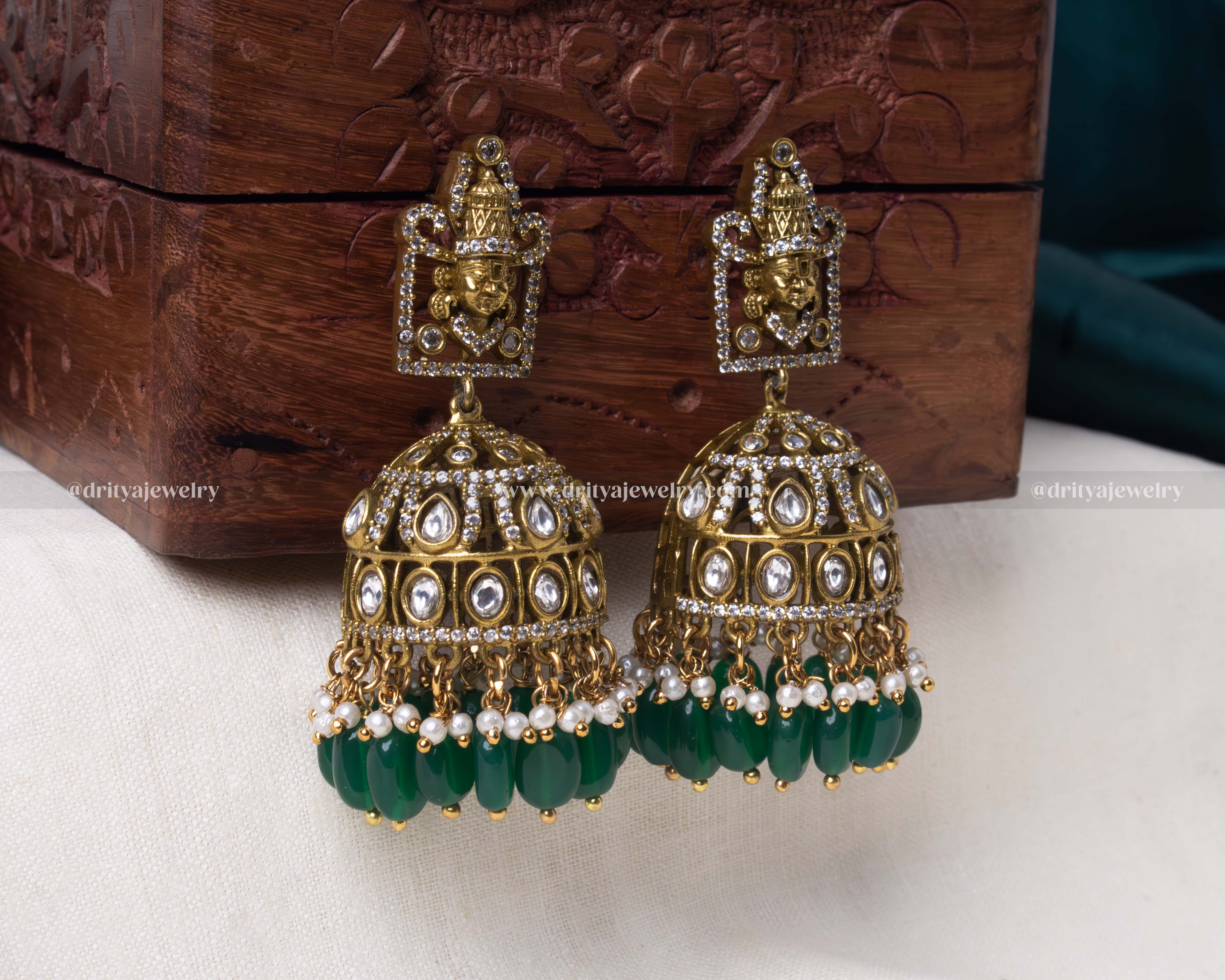 Close-up of dome-shaped jhumkas adorned with kundan stones, pearls, and green beads in Victorian polish.