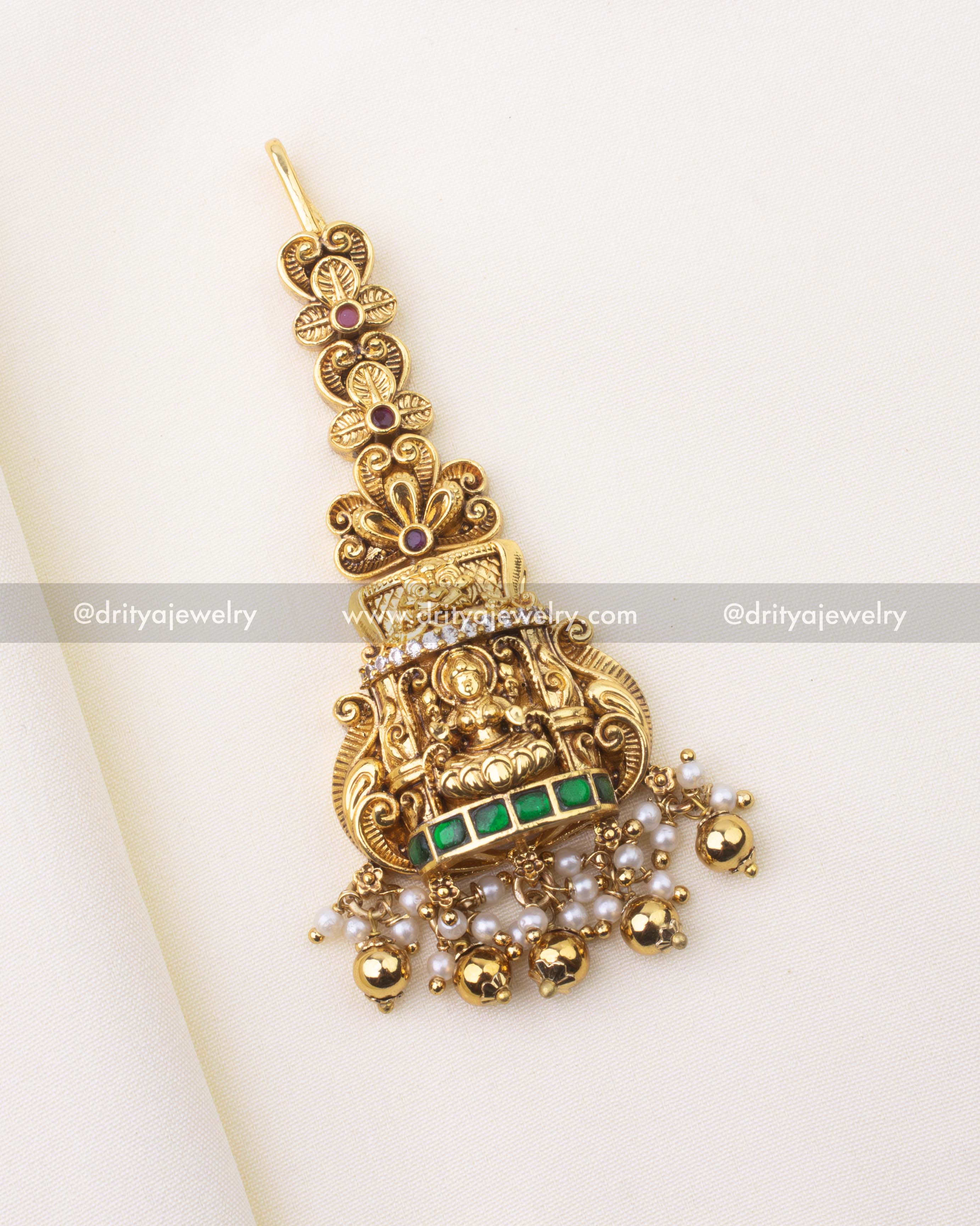 Temple-style Maang Tikka with Goddess Lakshmi motif, emerald Kemp stones, and pearl clusters.