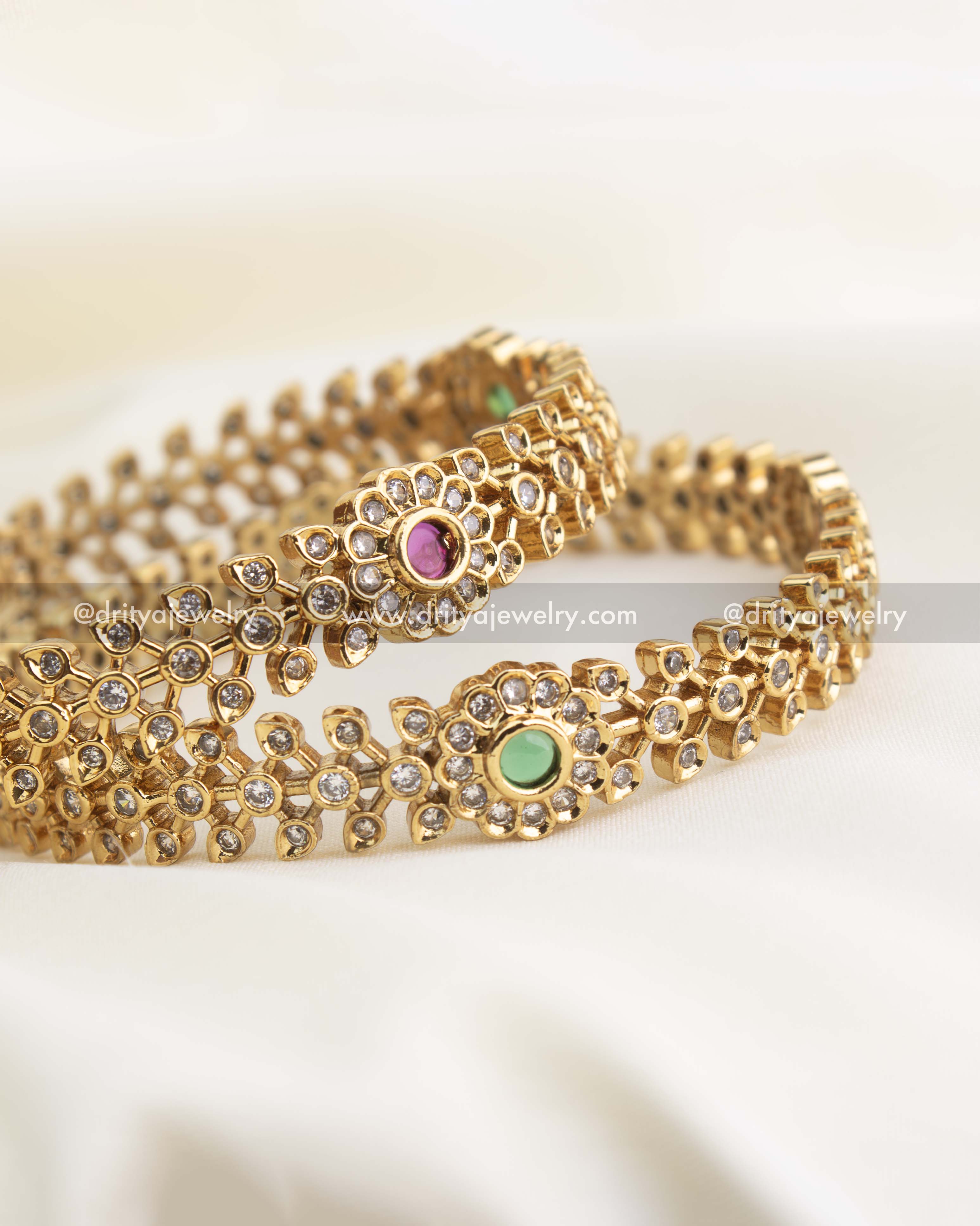 Detailed close-up of floral CZ bangles with ruby and green stones set in a gold replica finish by Dritya Jewelry.