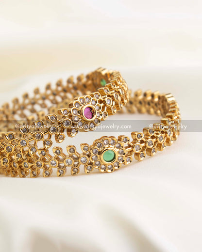 Detailed close-up of floral CZ bangles with ruby and green stones set in a gold replica finish by Dritya Jewelry.