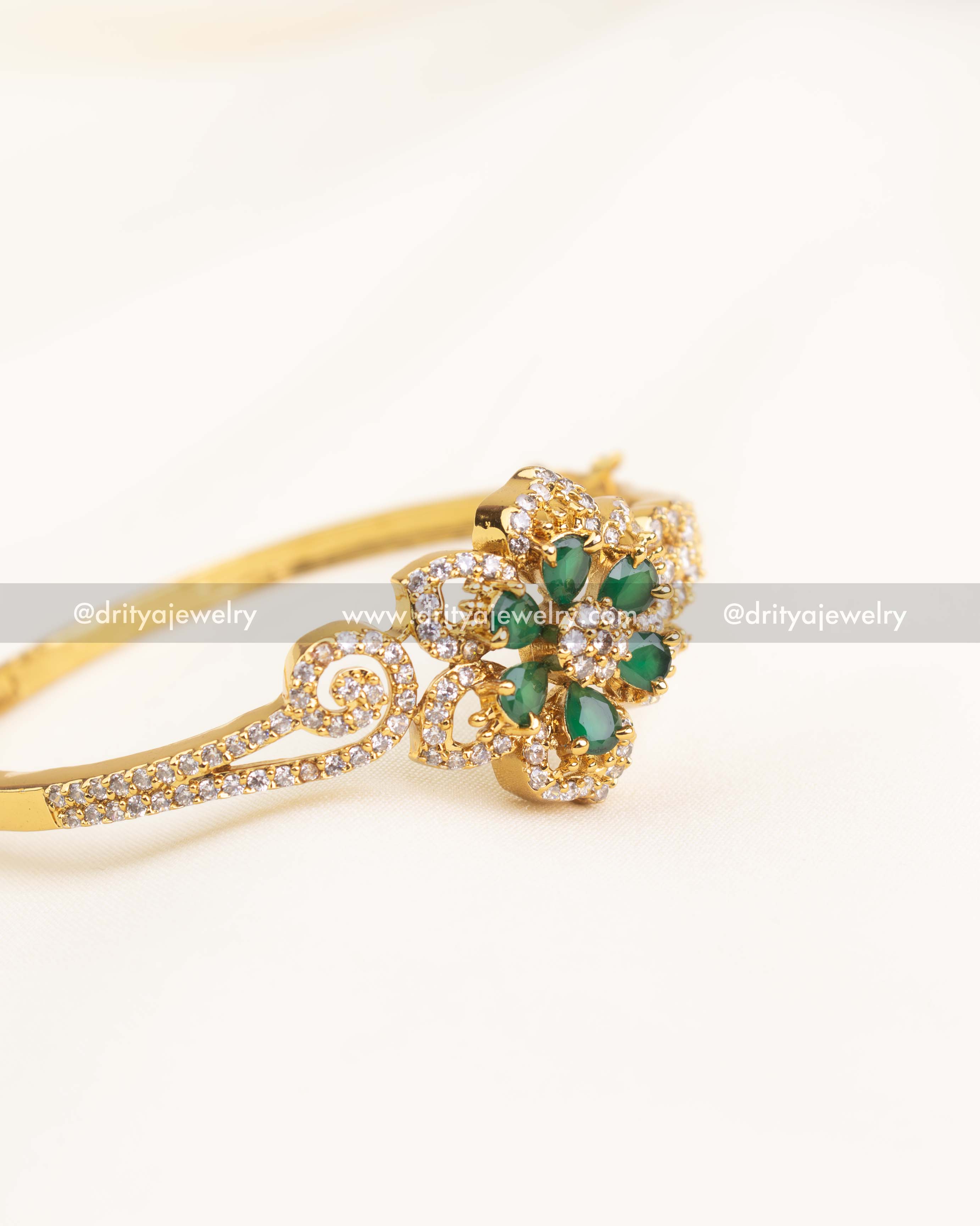 Openable gold kada with green teardrop stones arranged in a floral pattern.