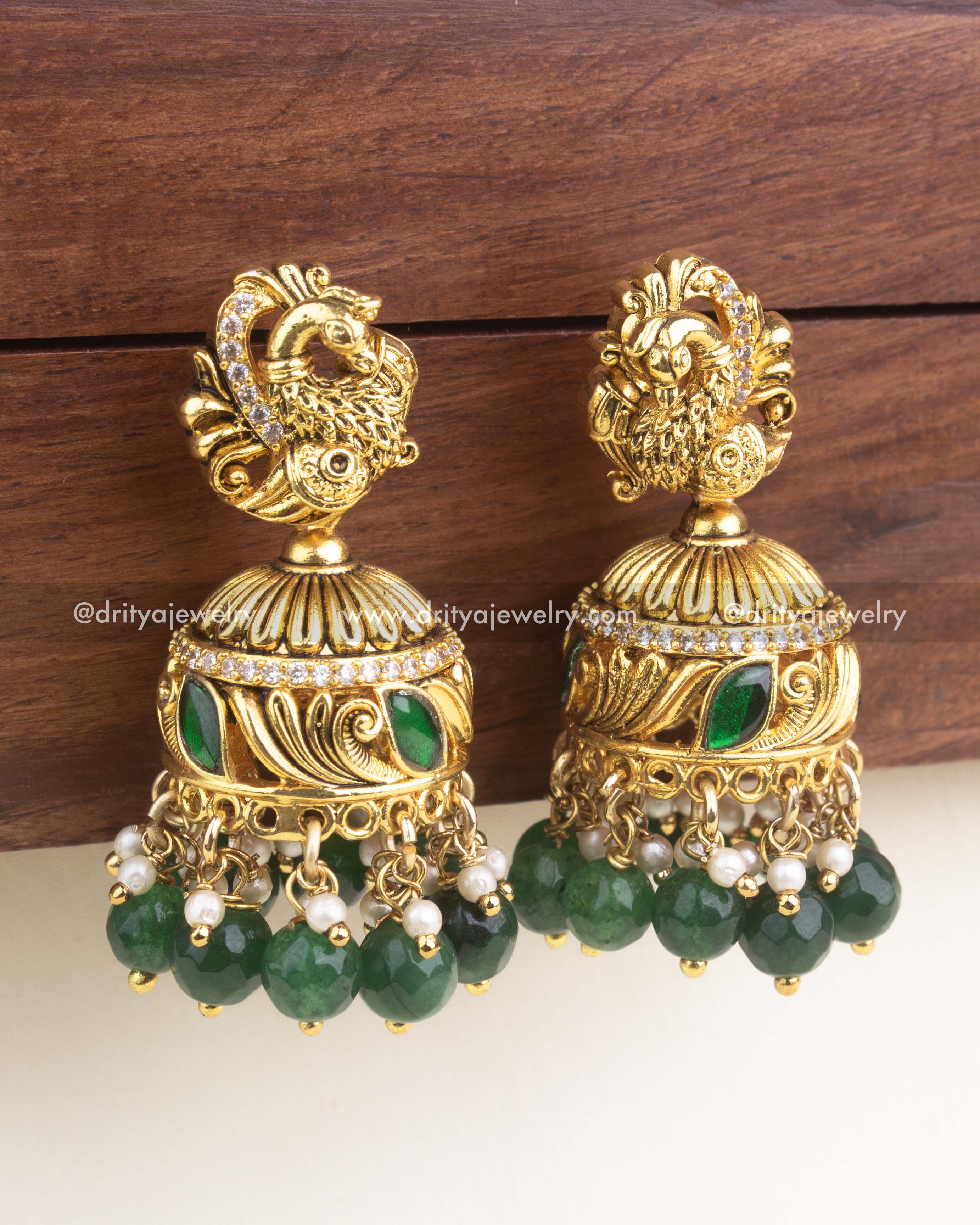Close-up of emerald green jadau jhumka showing enamel leaf work, CZ band, and faceted green beads.