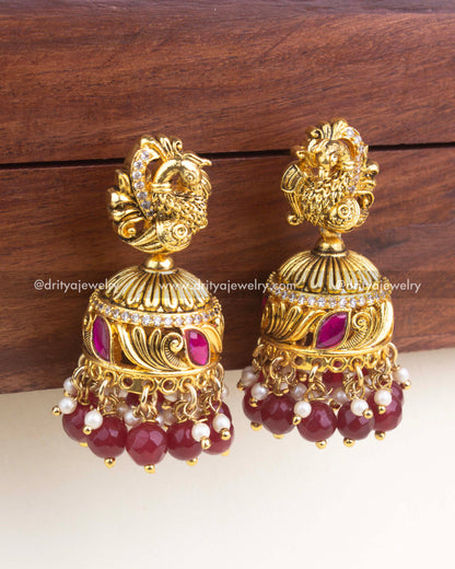 Close-up of ruby red jadau jhumka featuring carved details, CZ stones, red enamel, and pearl clusters.