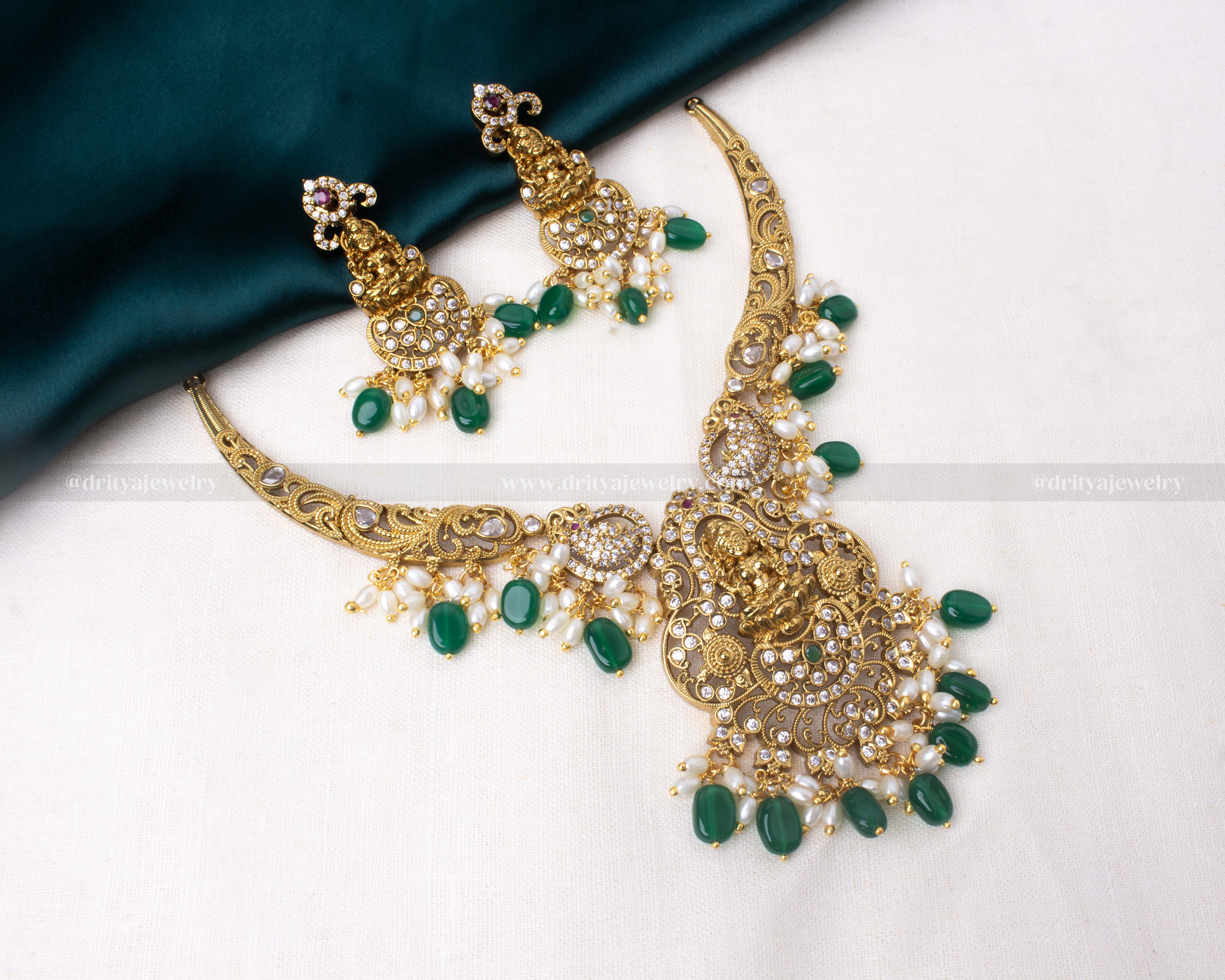 legant short necklace with Lakshmi motif, antique gold polish, and pearl and bead detailing, paired with matching earrings in emerald green or ruby red.