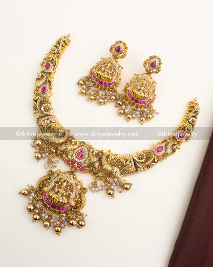 Antique gold temple short necklace with Lakshmi motif, ruby kemp stones, and matching dangler earrings from Dritya Jewelry.