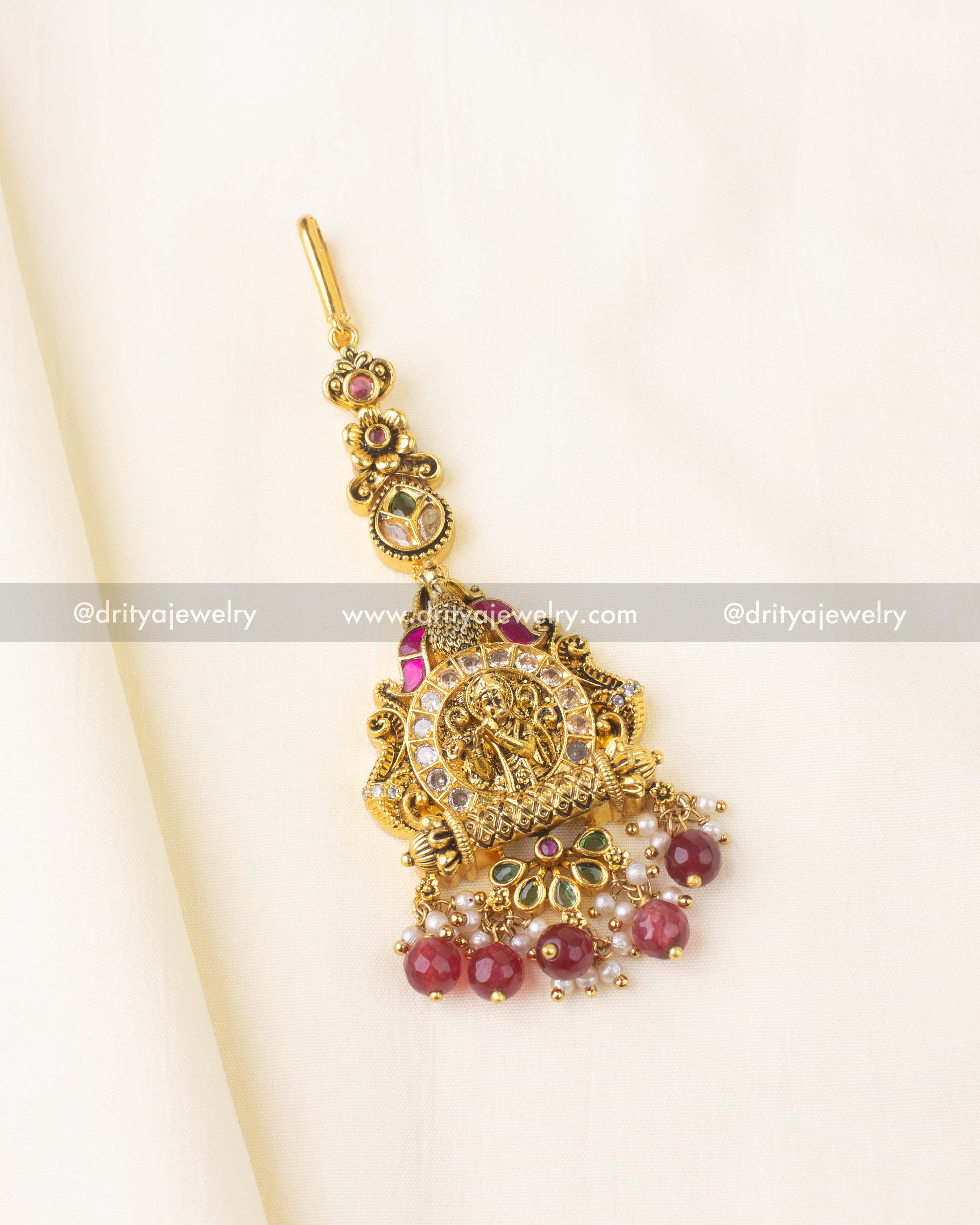 Temple-style maang tikka featuring Krishna motif, Kemp stones, and red bead drops