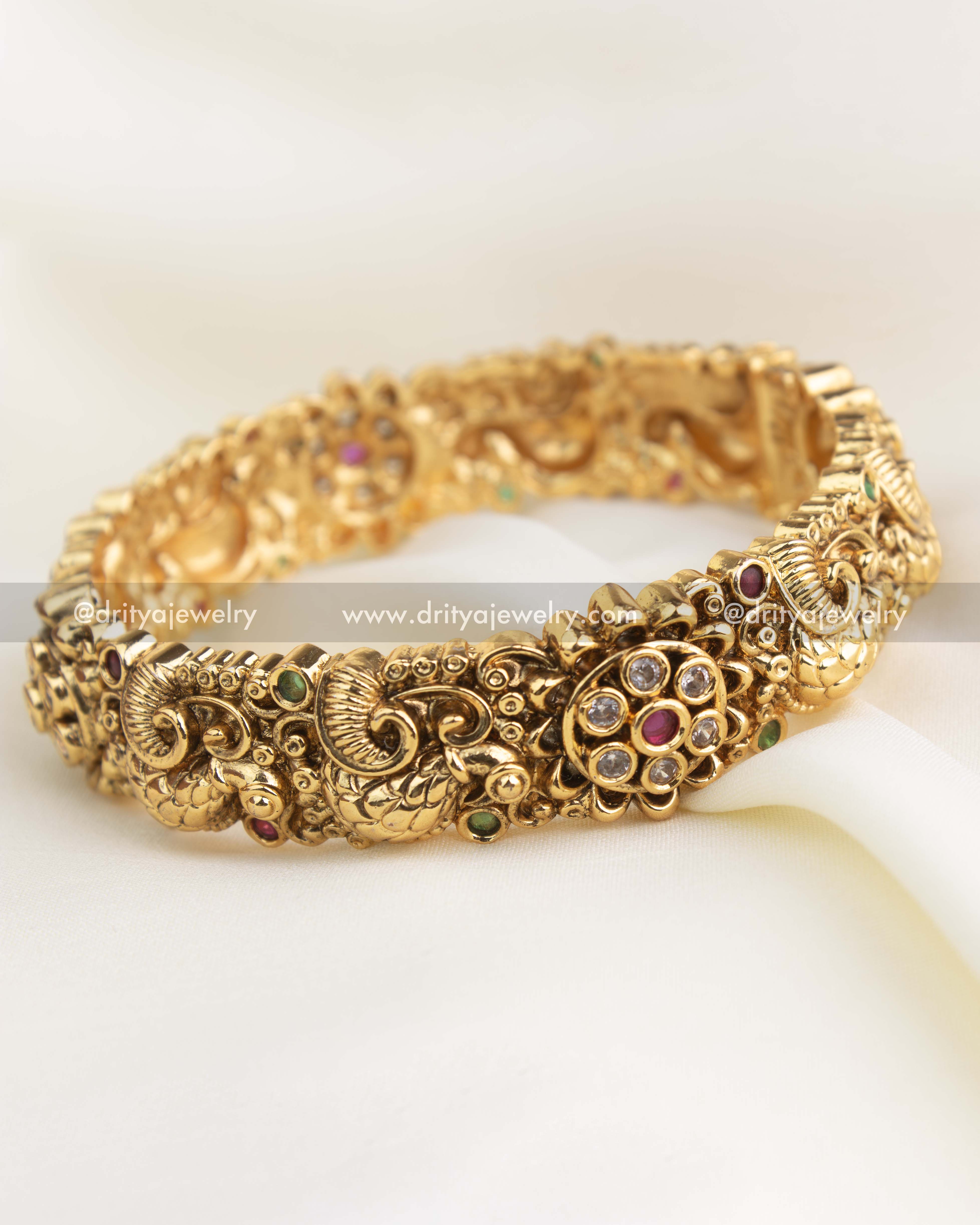 Antique gold openable bangle with peacock and floral Nakshi carvings, embedded with CZ and coloured stones.