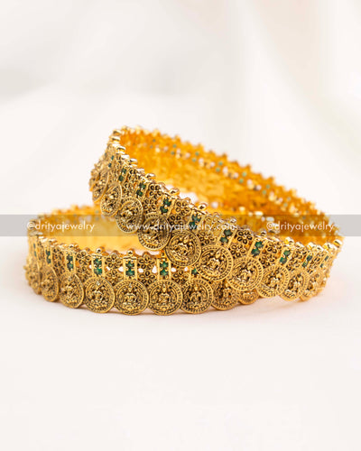 Close-up front view of antique gold nakshi bangles with green stones and coin motifs.