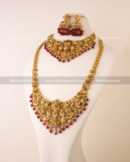 Bridal Nakshi jewelry set featuring long necklace, short necklace, jhumkas, and maang tikka with ruby beads and antique gold finish.