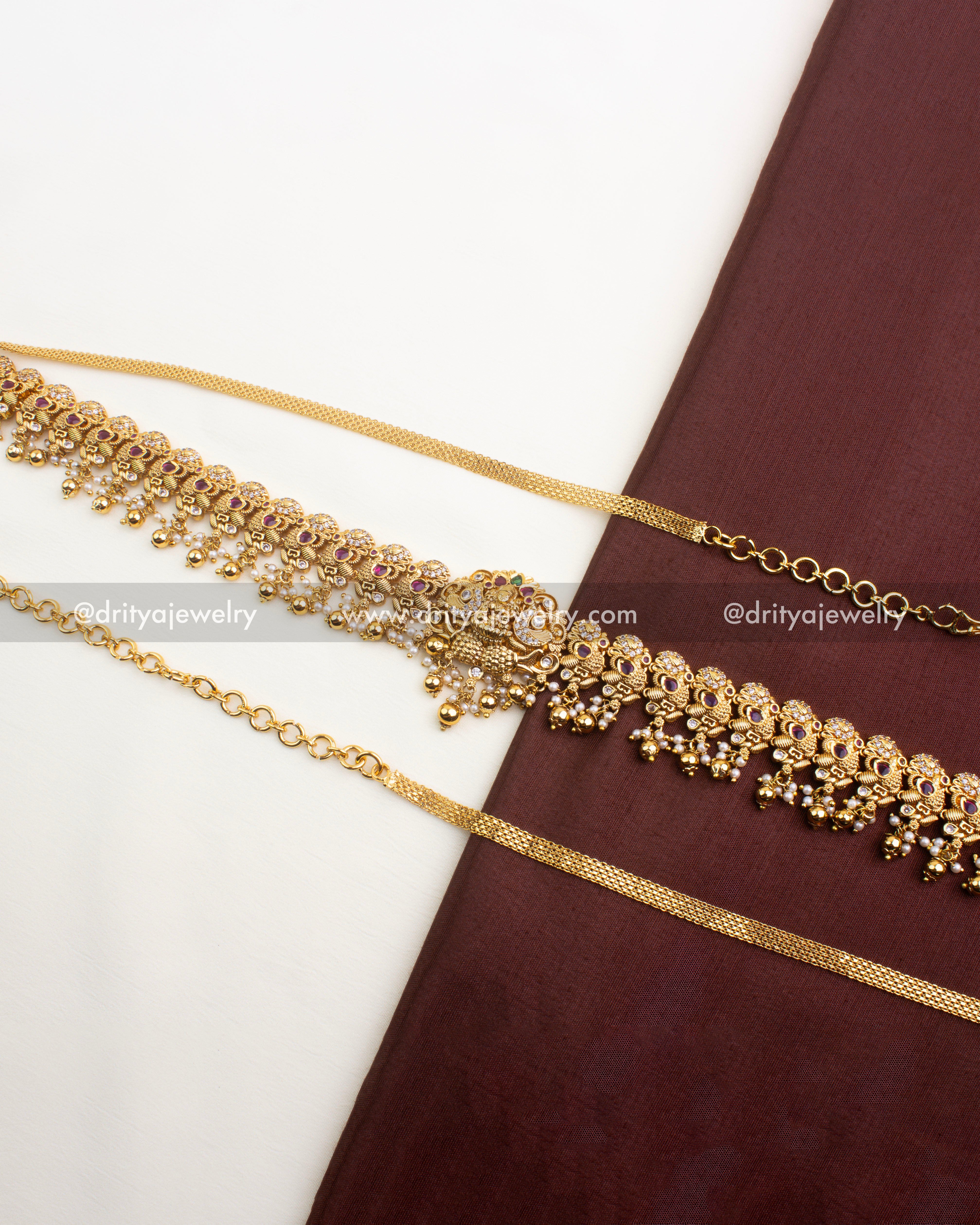 Full view of antique gold Nakshi hip chain with ruby red stones and pearl drops, displayed on fabric background.