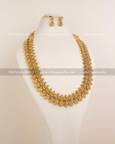 Temple-style long haram with Lakshmi motifs and green stones in antique gold finish.
