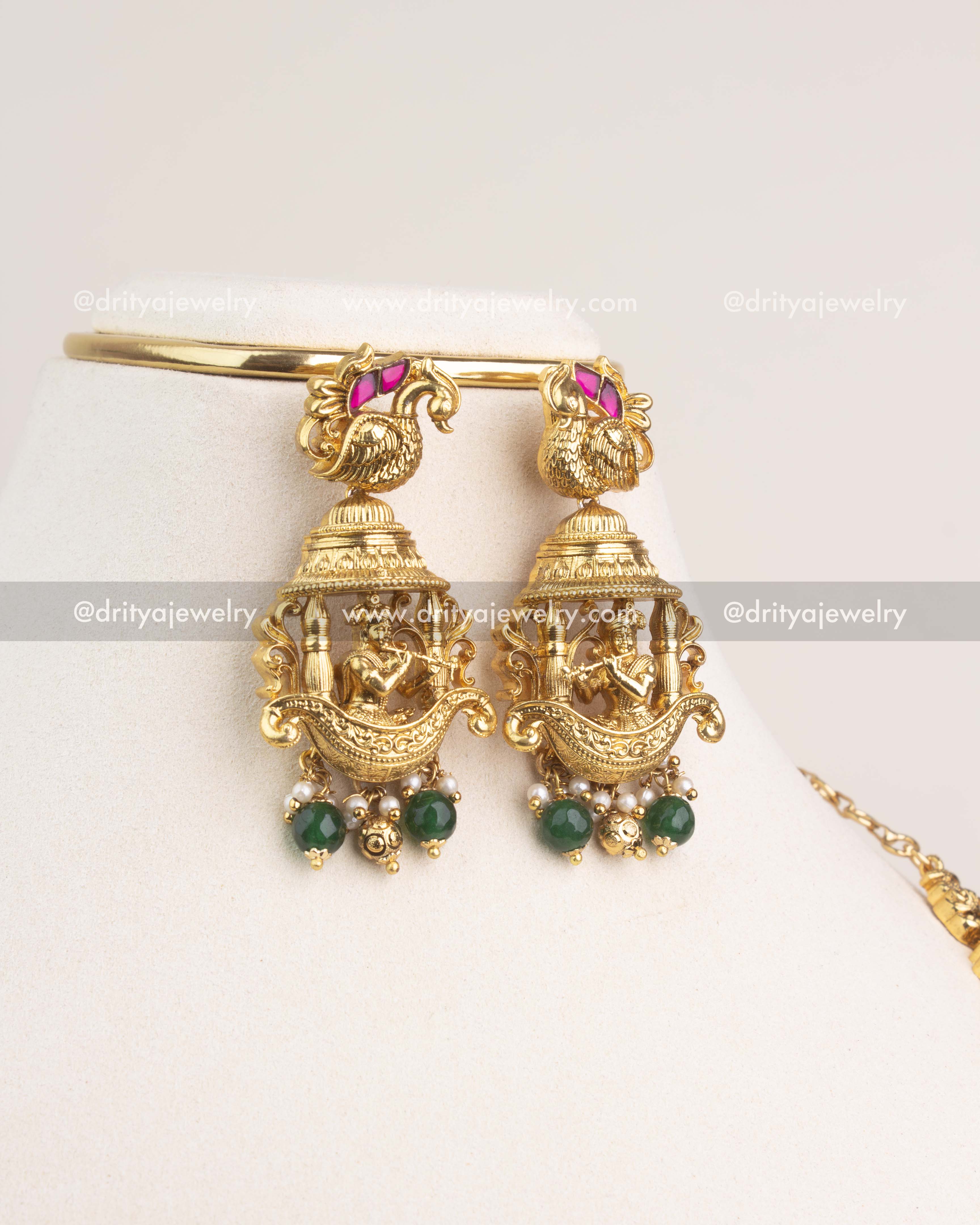 Matching temple jhumka earrings with Krishna motif and green bead danglings.