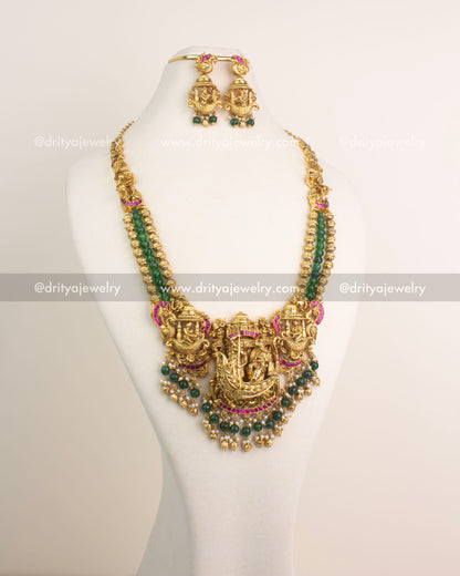 Antique gold Nakshi long haram featuring Lord Krishna boat motif with ruby Kemp stones and emerald green bead hangings.