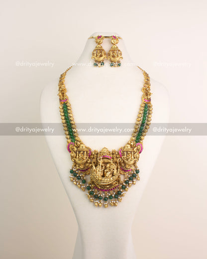 Antique gold Nakshi long haram featuring Lord Krishna boat motif with ruby Kemp stones and emerald green bead hangings.