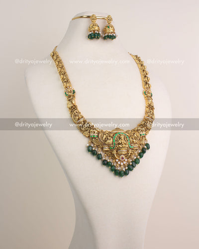Temple-inspired long necklace with Lakshmi Devi pendant, green Jadau stones, and antique gold finish.
