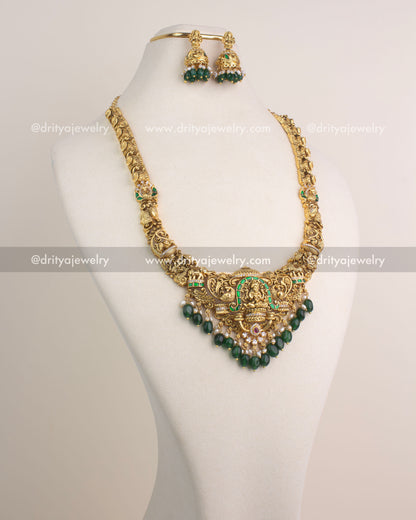 Temple-inspired long necklace with Lakshmi Devi pendant, green Jadau stones, and antique gold finish.