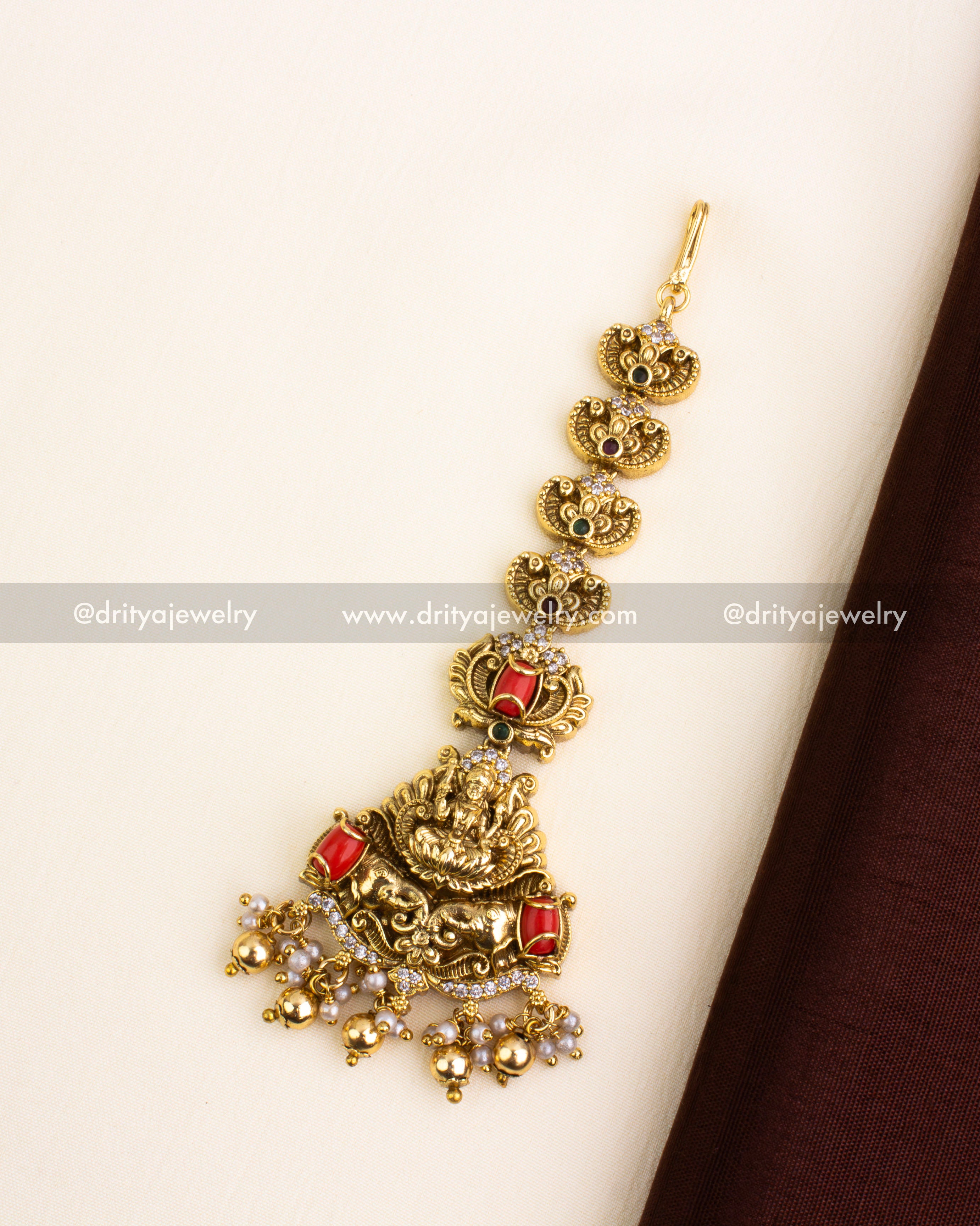 Traditional gold-plated Nakshi maang tikka featuring coral red stones, Lakshmi motif, and bead drops.