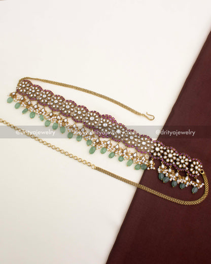 Antique gold Polki Kundan hip chain with floral motifs, ruby accents, and green bead drops from Dritya Jewelry.