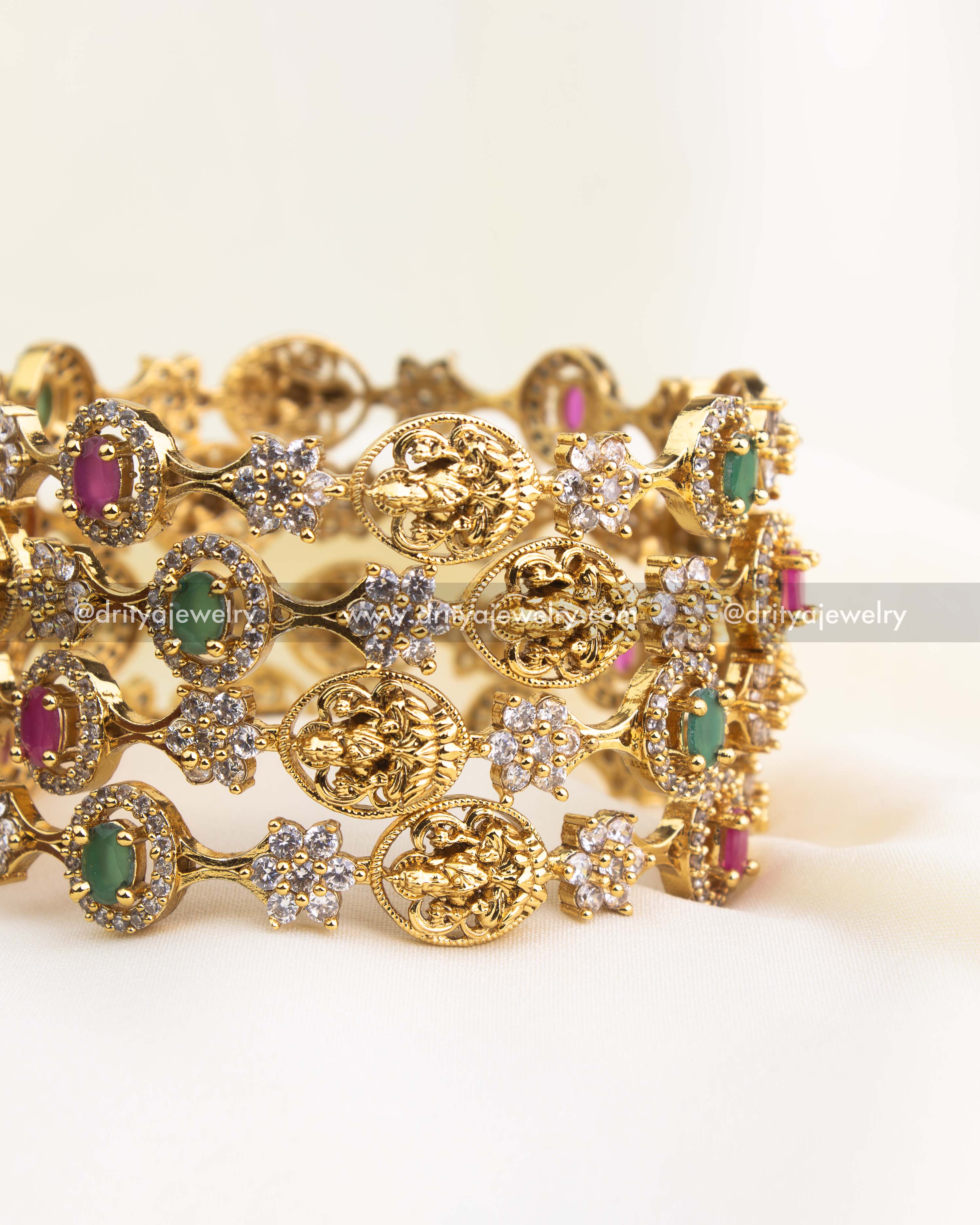 Gold-finished temple bangles featuring ruby and emerald stones with Lakshmi motifs and CZ detailing from Dritya Jewelry.