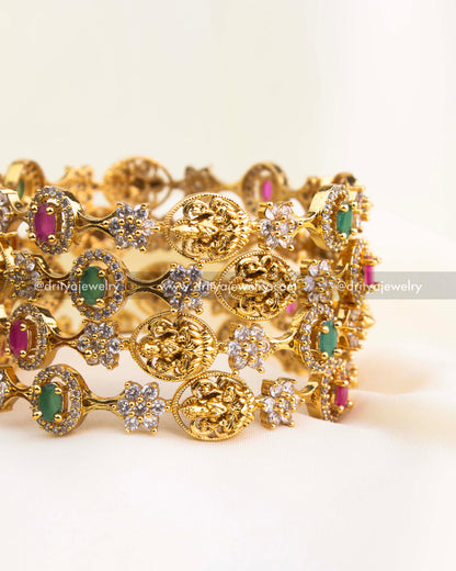 Gold-finished temple bangles featuring ruby and emerald stones with Lakshmi motifs and CZ detailing from Dritya Jewelry.