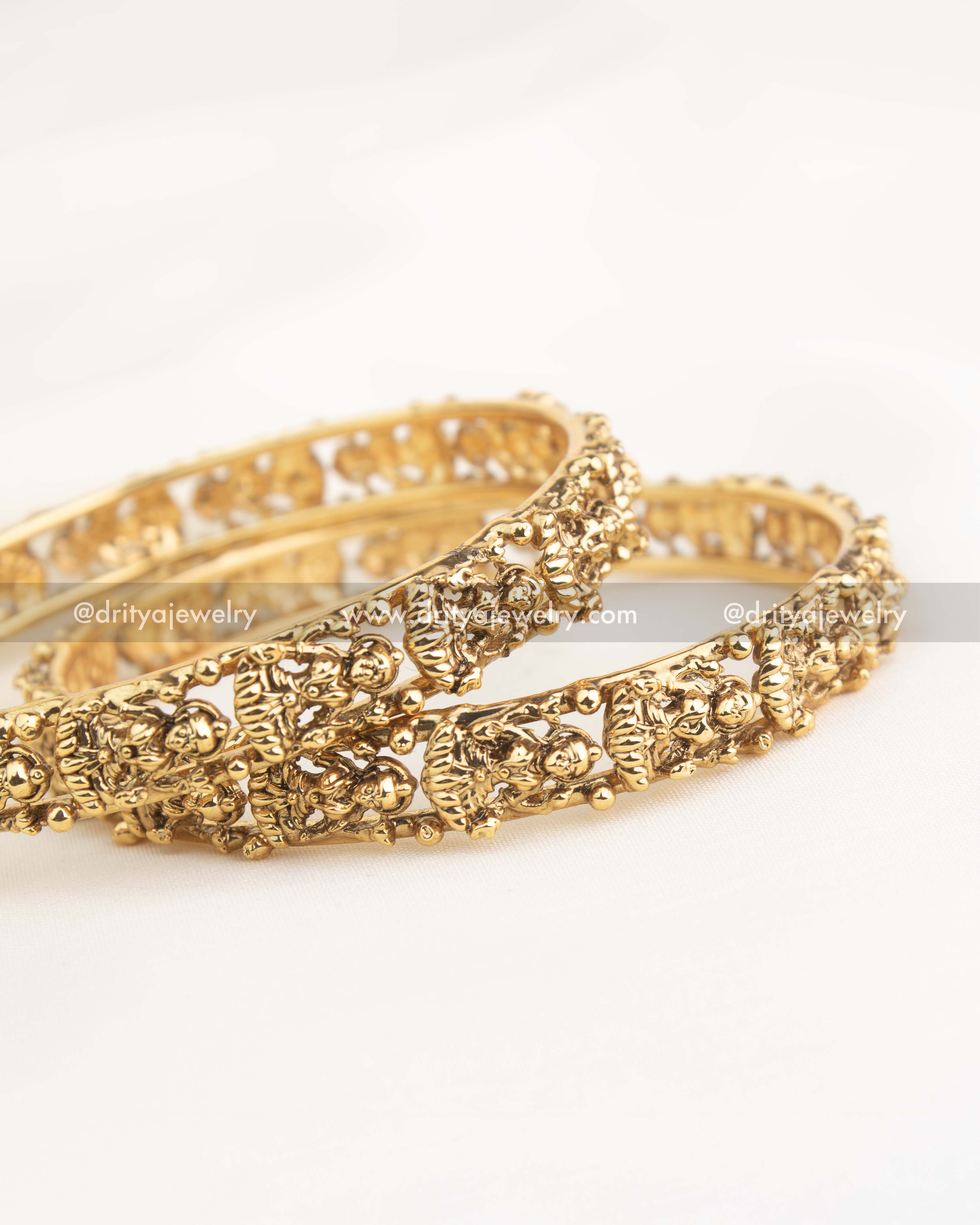 Close-up of openwork carving and Lakshmi idol detailing on gold-plated temple bangles.