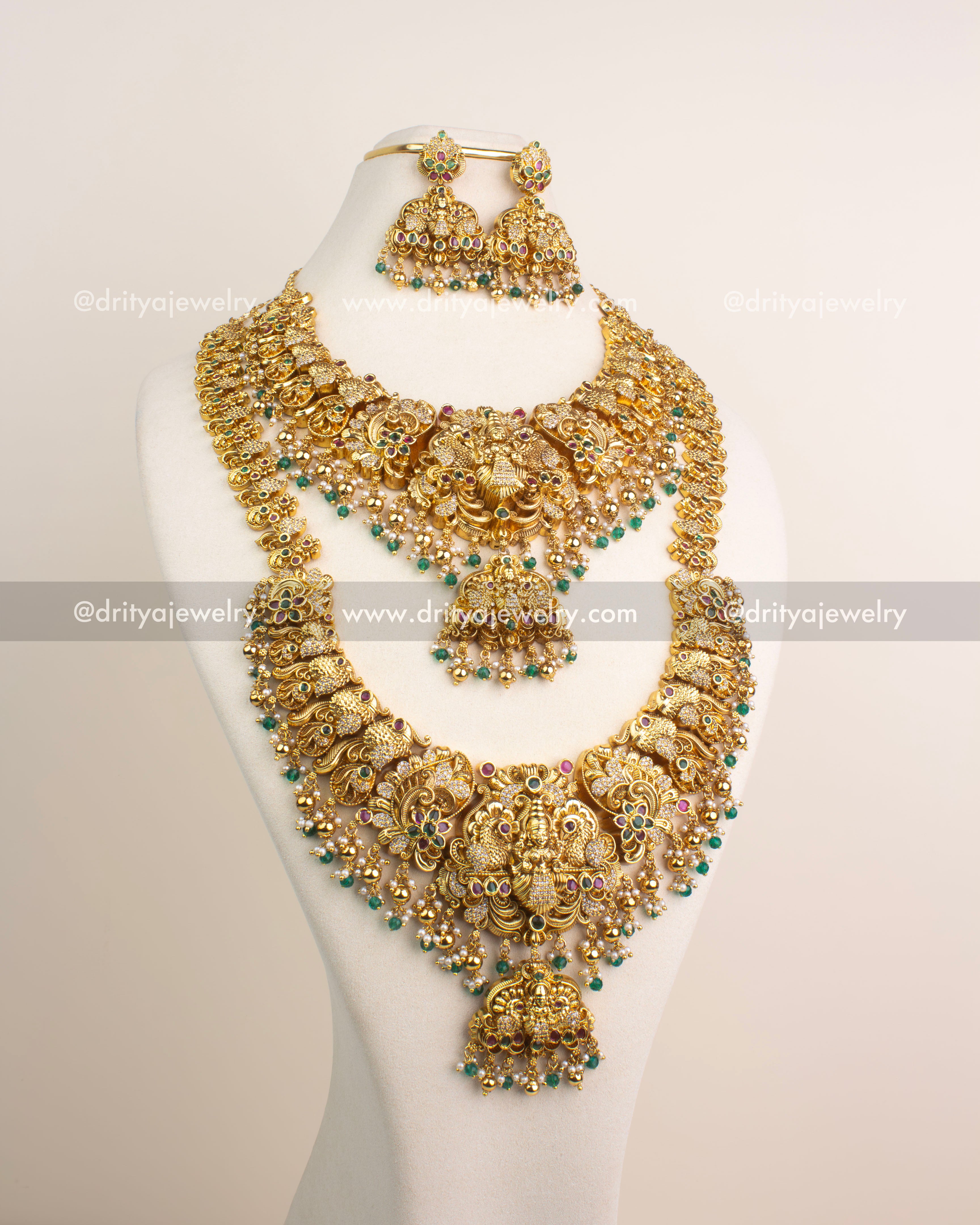 Antique gold temple bridal jewelry set with Lakshmi Devi motifs and emerald green bead hangings, includes long necklace, short necklace, earrings and maang tikka.