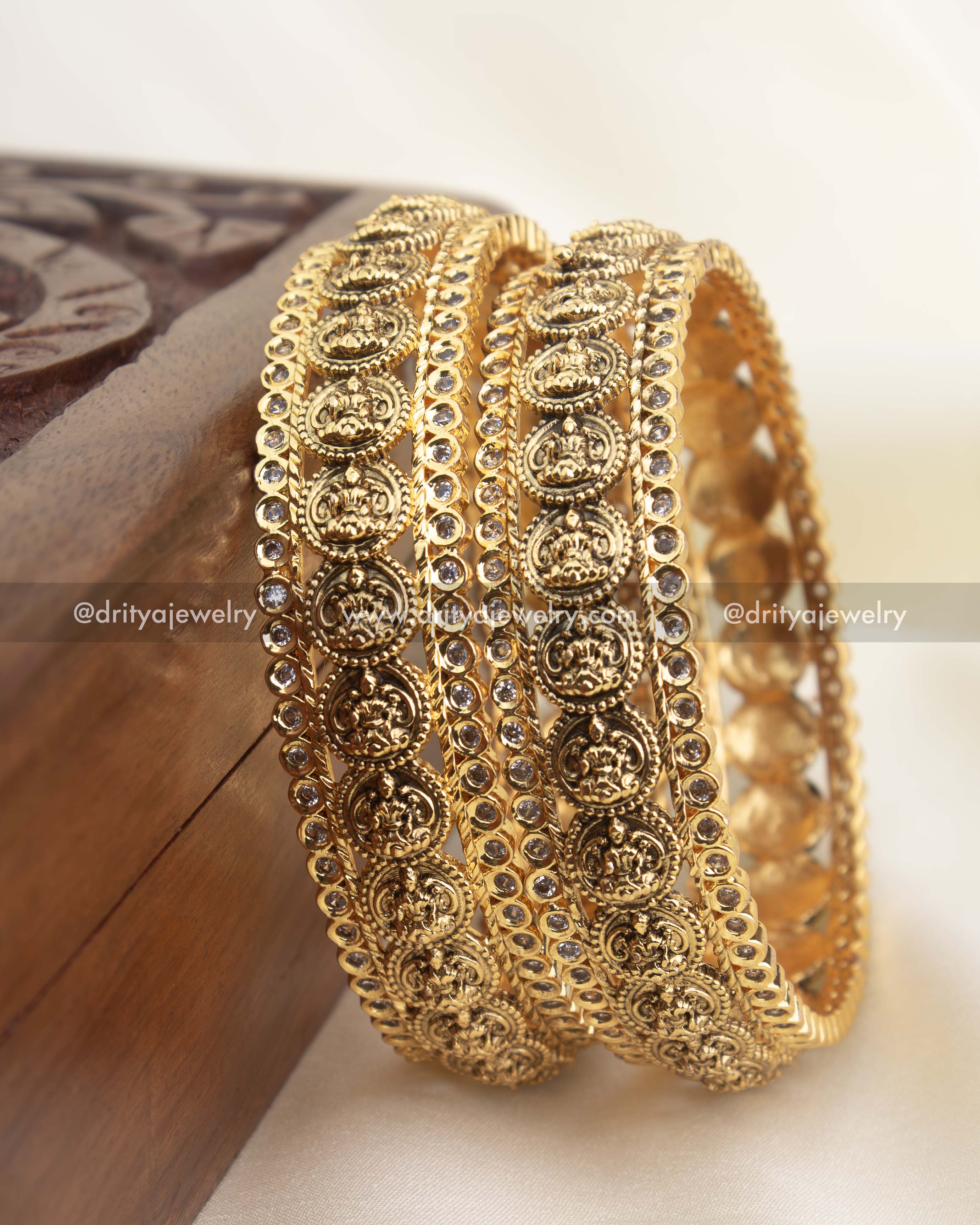 High-gold temple bangles with repeating Lakshmi coin motifs and CZ stone borders.