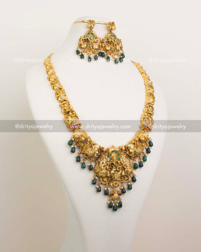 Long antique gold haram featuring Krishna-Parvati pendant and emerald green bead drops.