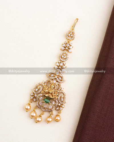 Temple-style maang tikka with green stone centerpiece, CZ accents, and pearl drops.