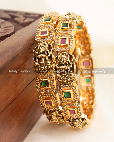 High-gold temple bangles with Nakshi deity panels and alternating green and ruby square stones.