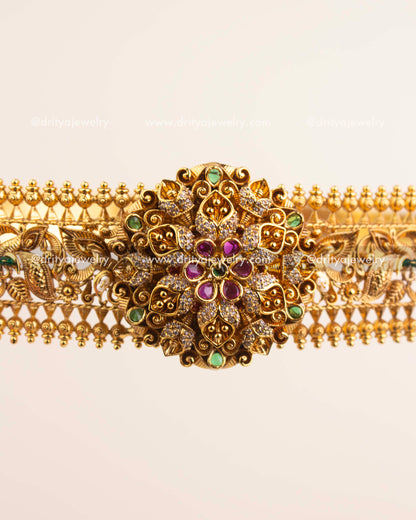 Handcrafted floral centerpiece of vadanam featuring ruby and emerald stones in antique gold finish.