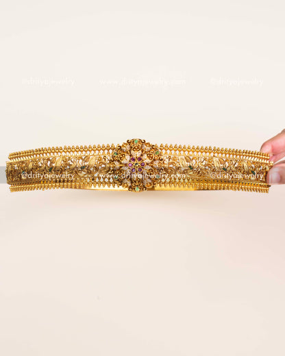 Antique gold traditional vadanam with floral centerpiece, ruby and emerald stone detailing.